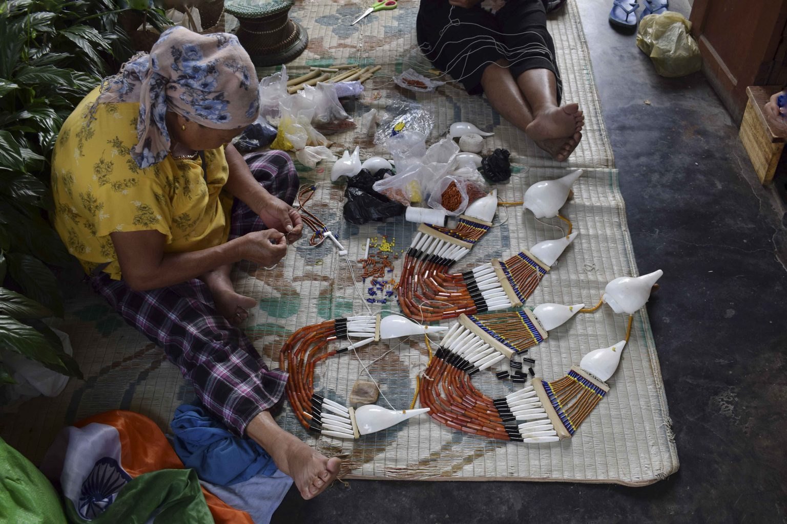 A woman stringing Rengma beaded necklaces on a mat, with finished pieces laid out beside her