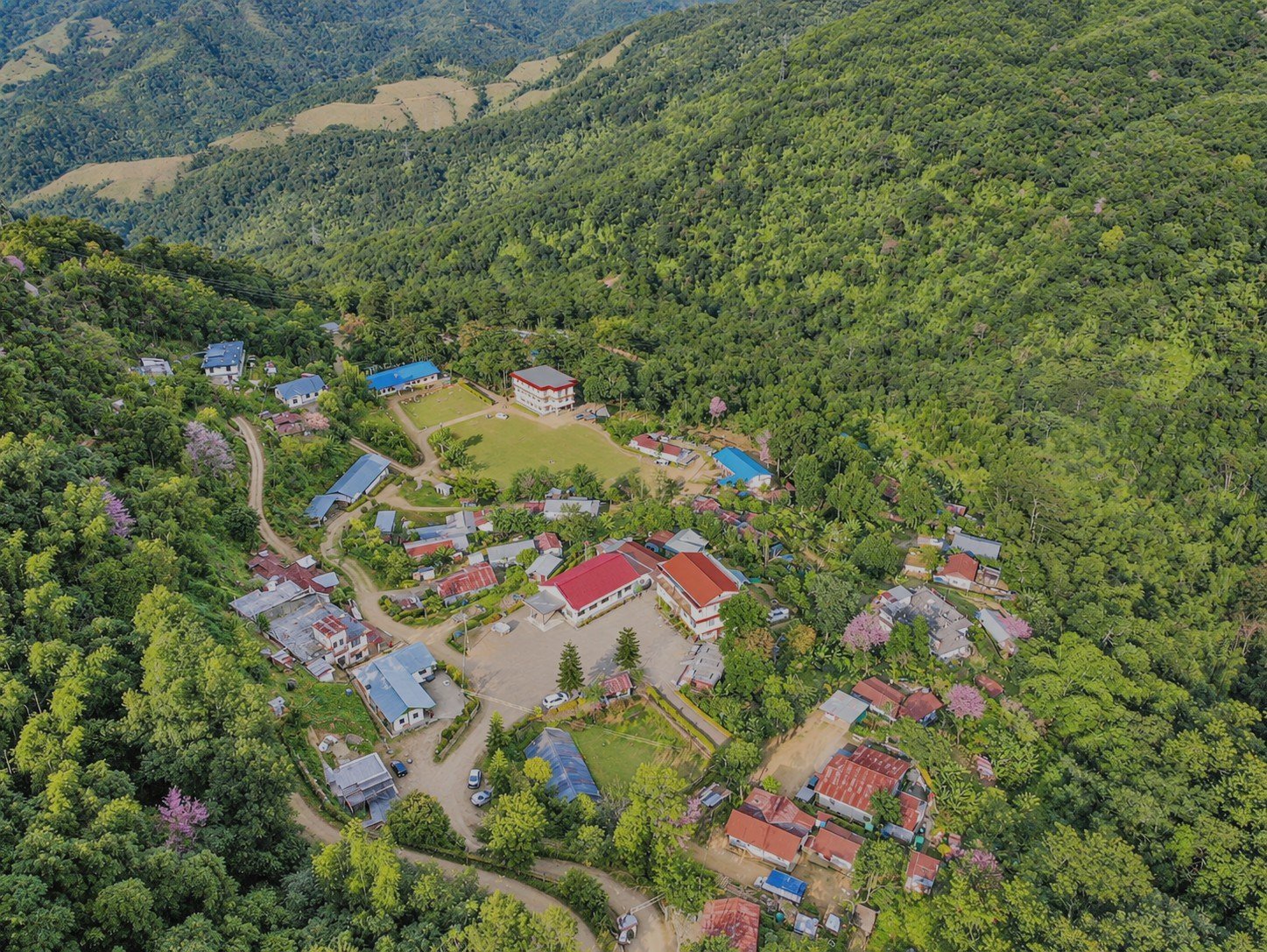 Zunpha and the cooperative campus seen from the air, its buildings and playing field set in forested hills