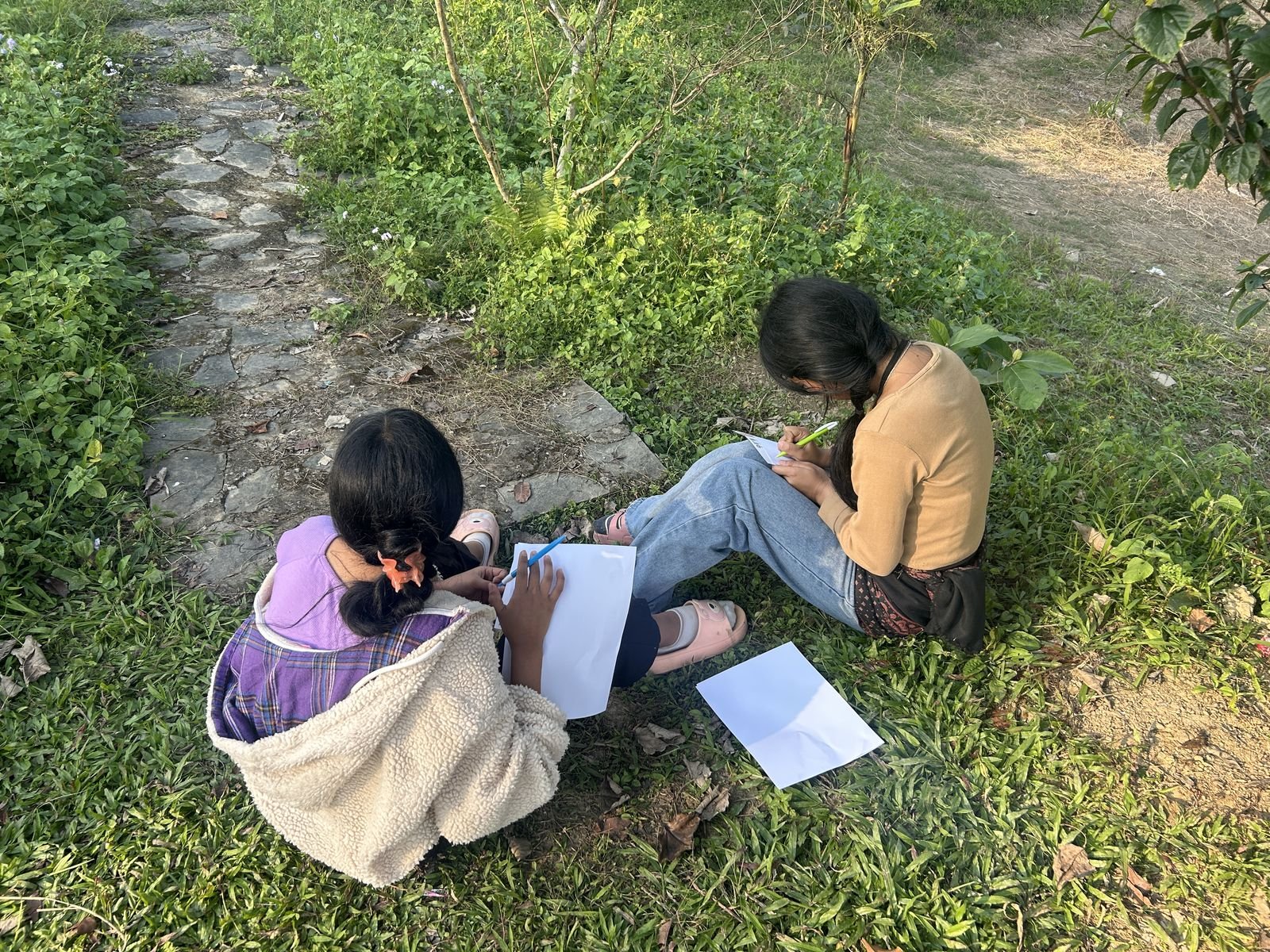 Two girls sitting on the grass writing field notes