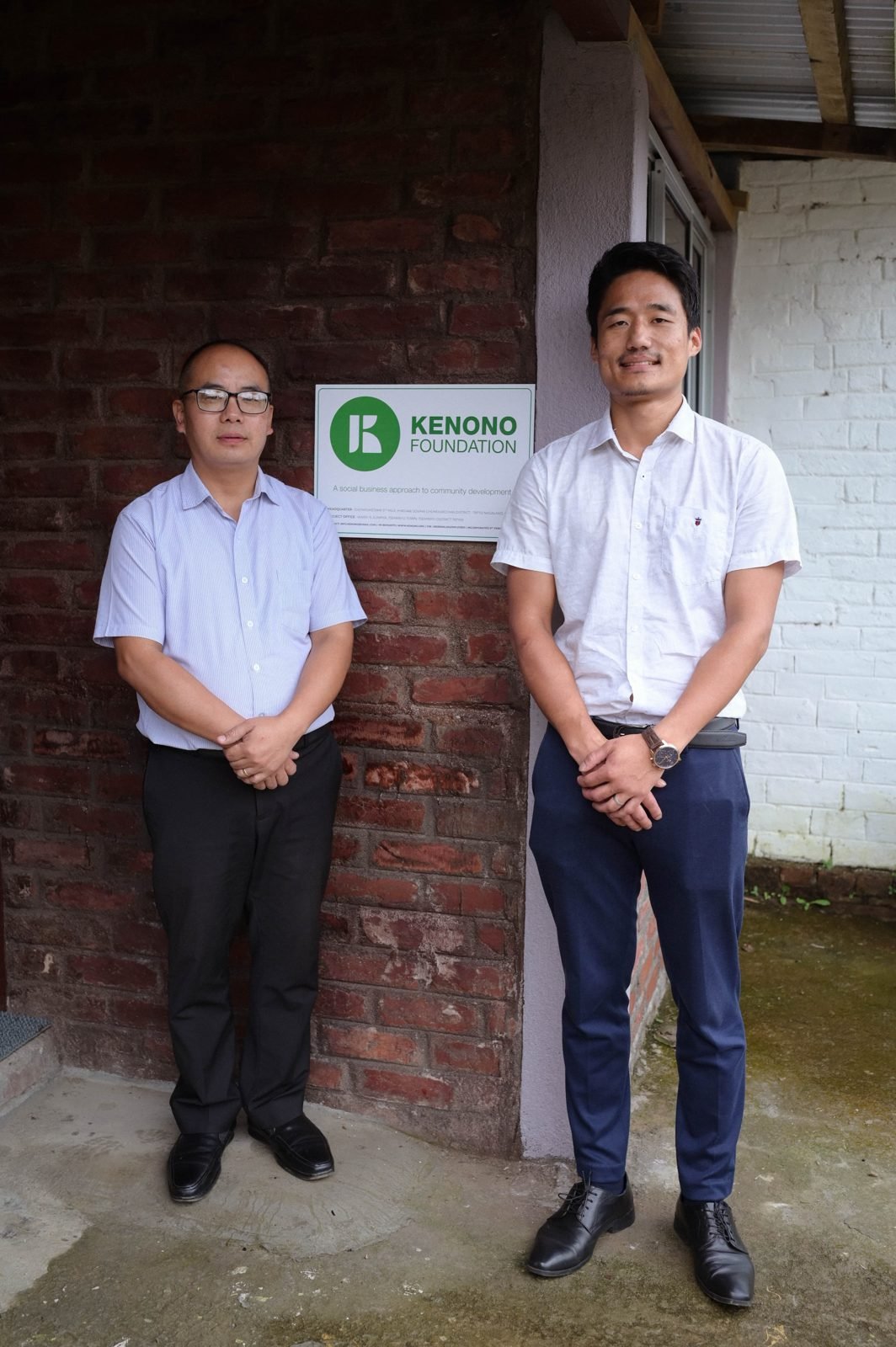 Haiwalo Apon and Ruchinilo Kemp standing either side of the Kenono Foundation sign on a brick wall